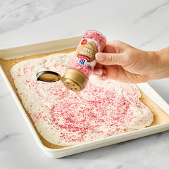 Sprinkling McCormick Candy Cane Finishing Sugar over white chocolate bark on a baking sheet
