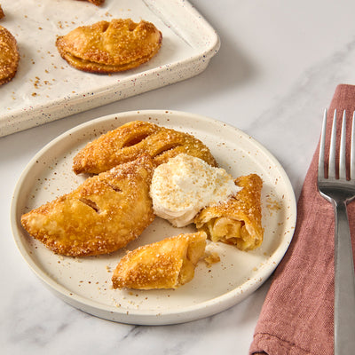 Apple pie turnovers on a plate with a side of ice cream, served on a marble surface.