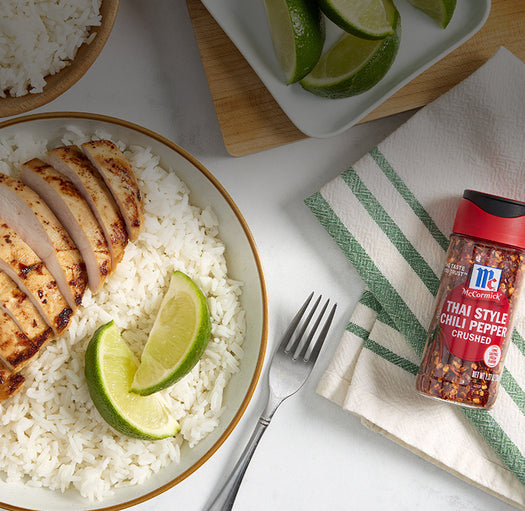 sliced chicken on a bed of rice with lemon and crushed thai style chili pepper