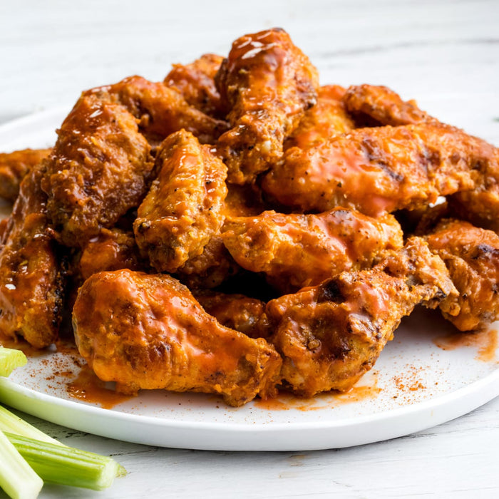 A plate of chicken wings covered in sauce with celery sticks on the side.