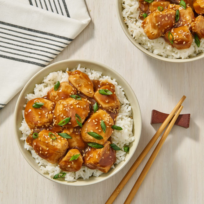 A bowl of teriyaki chicken with sesame seeds and green onions served over white rice.