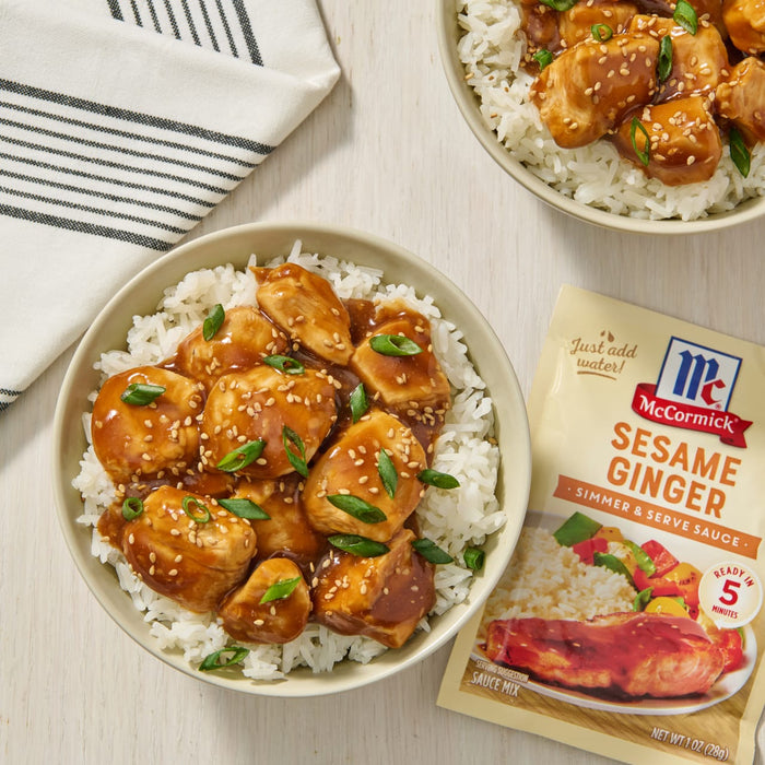 A bowl of white rice topped with sesame ginger chicken and green onions, next to a McCormick Sesame Ginger Simmer & Serve Sauce packet.