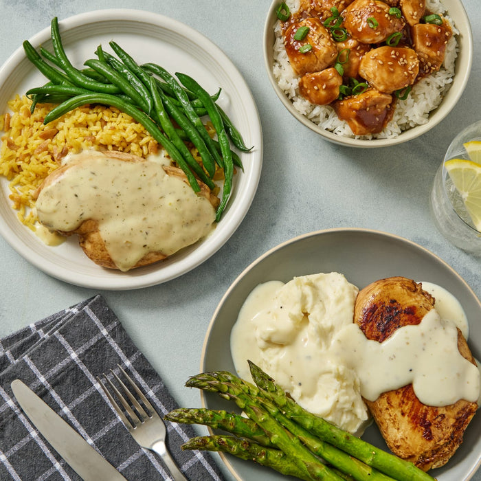 A table setting with three plates of food, one with chicken and rice, one with chicken and mashed potatoes, and one with chicken and green beans.
