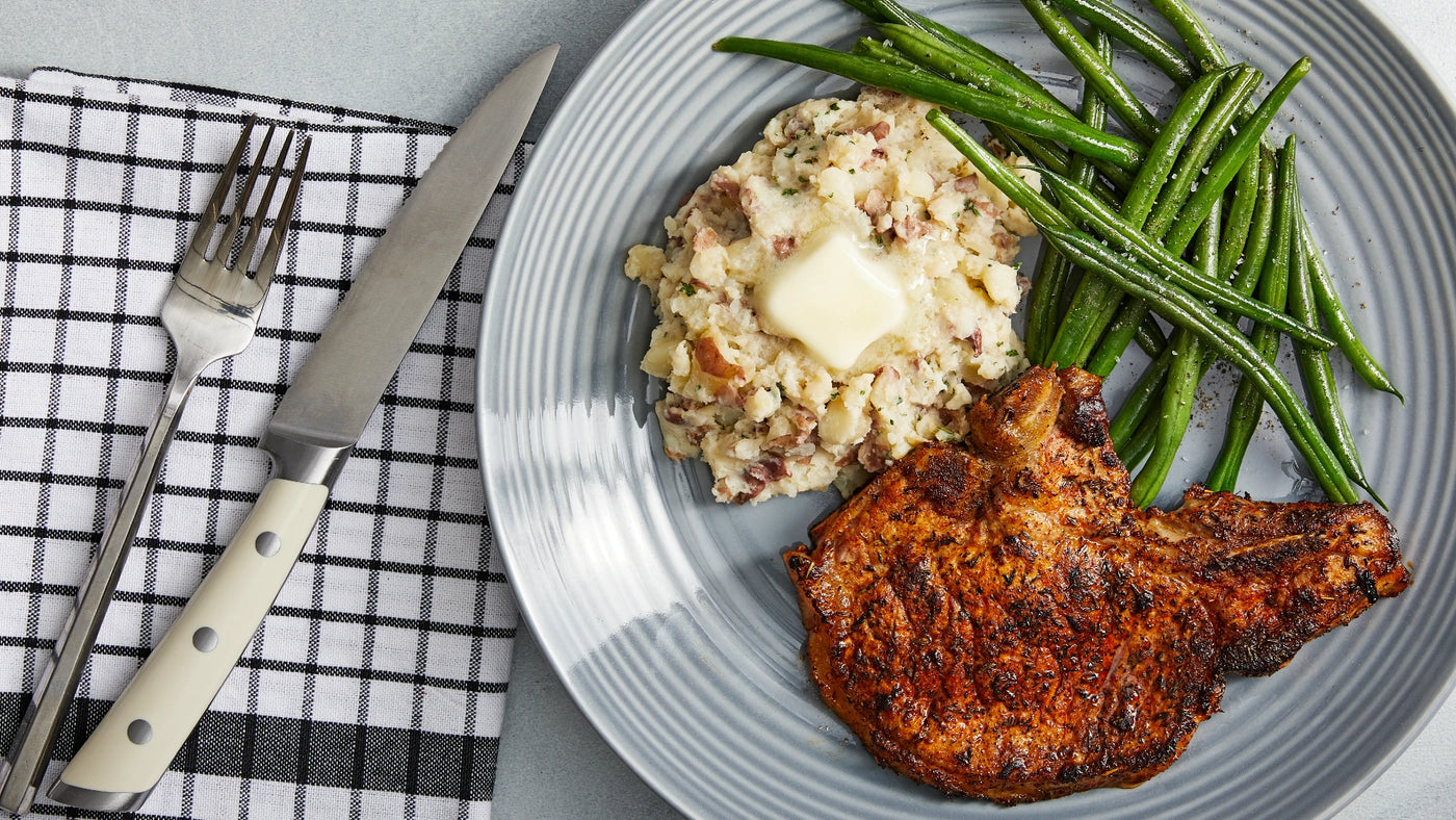 Grilled pork chop with mashed potatoes, green beans, and butter on a plate.