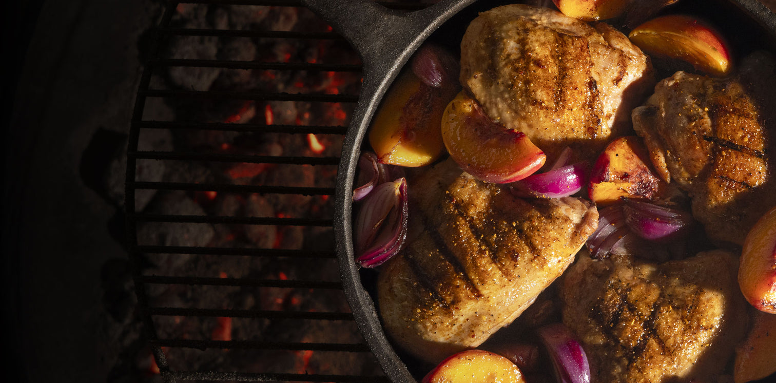 Chicken in a cast iron pan with onions and peaches over hot coals on a grill