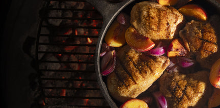 Chicken in a cast iron pan with onions and peaches over hot coals on a grill