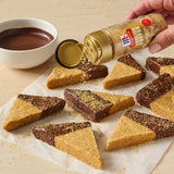 Person sprinkling McCormick English toffee finishing sugar on chocolate-dipped triangular cookies.
