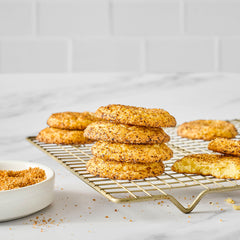 Stack of spiced orange sugar cookies on a cooling rack with one cookie partially eaten and spiced orange finishing sugar in a bowl nearby