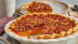 Pecan pie with a slice taken out on a white plate, placed on a wooden table.