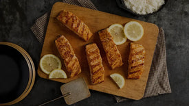 Grilled salmon fillets on a wooden board with lemon slices, served with a side of white rice.