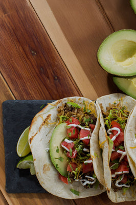 tacos with tomatoes, cheese, and avocado on a stone plate