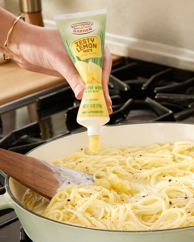 Zesty Lemon Paste squeezing into a pan of spaghetti