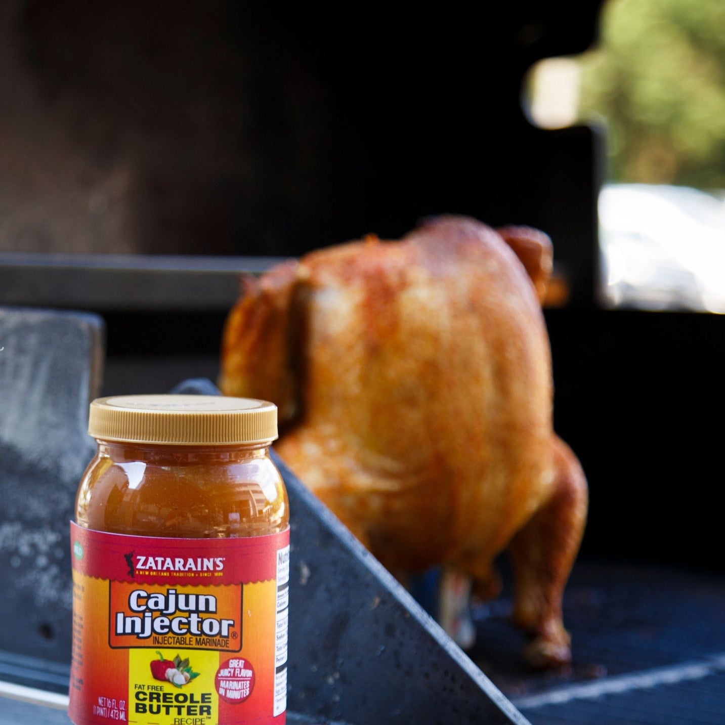zatarains cajun injector with a background of a chicken on a blackstone in the background