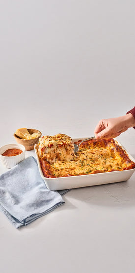 A close-up of a lasagna dish with a serving being lifted out with a spatula.