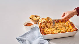 A close-up of a lasagna dish with a serving being lifted out with a spatula.