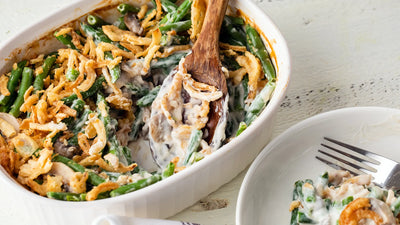 Green bean casserole with crispy fried onions in a white baking dish, served with a wooden spoon.