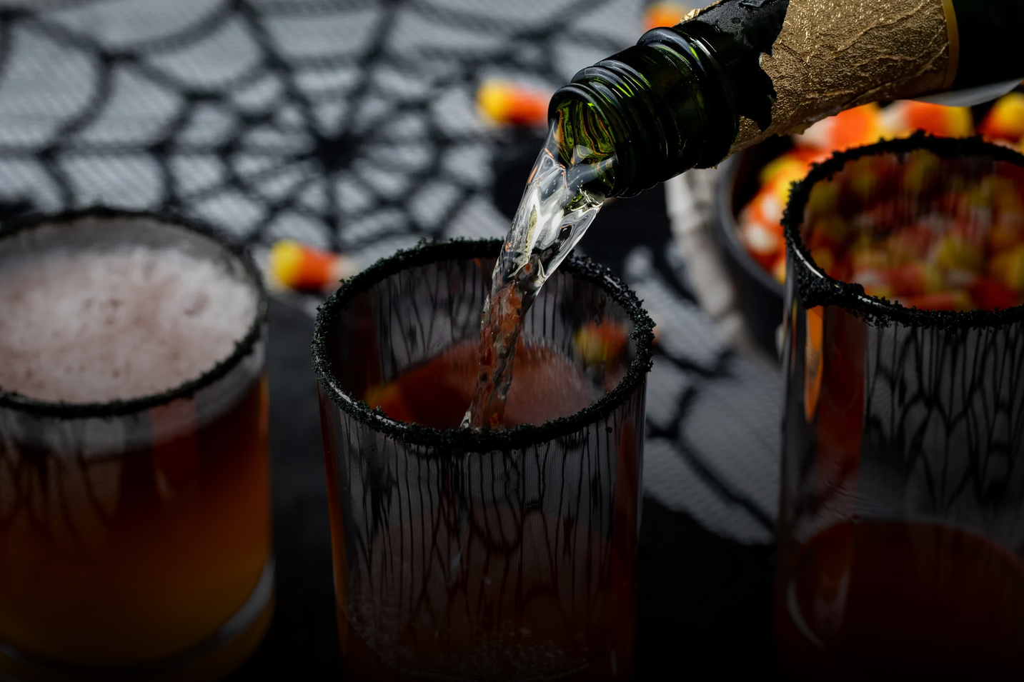 Pouring a drink into a glass with Halloween-themed decorations in the background