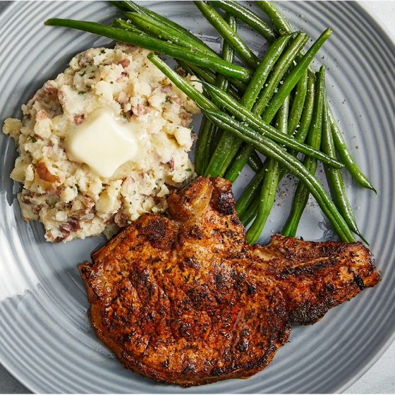 Grilled pork chop with mashed potatoes, green beans, and butter on a plate.