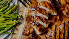 sliced grilled hickoy brown sugar chicken on a wooden board with asparagus