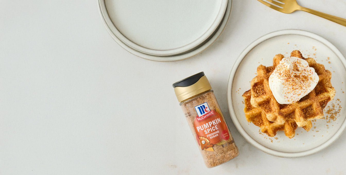 Pumpkin spice seasoning bottle next to a plate of waffles with whipped cream on a light background
