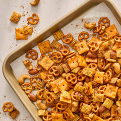Assorted snack mix including pretzels, crackers, and nuts on a baking tray.
