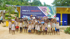Children holding up packages in front of a 'Merci Misadtra' banner