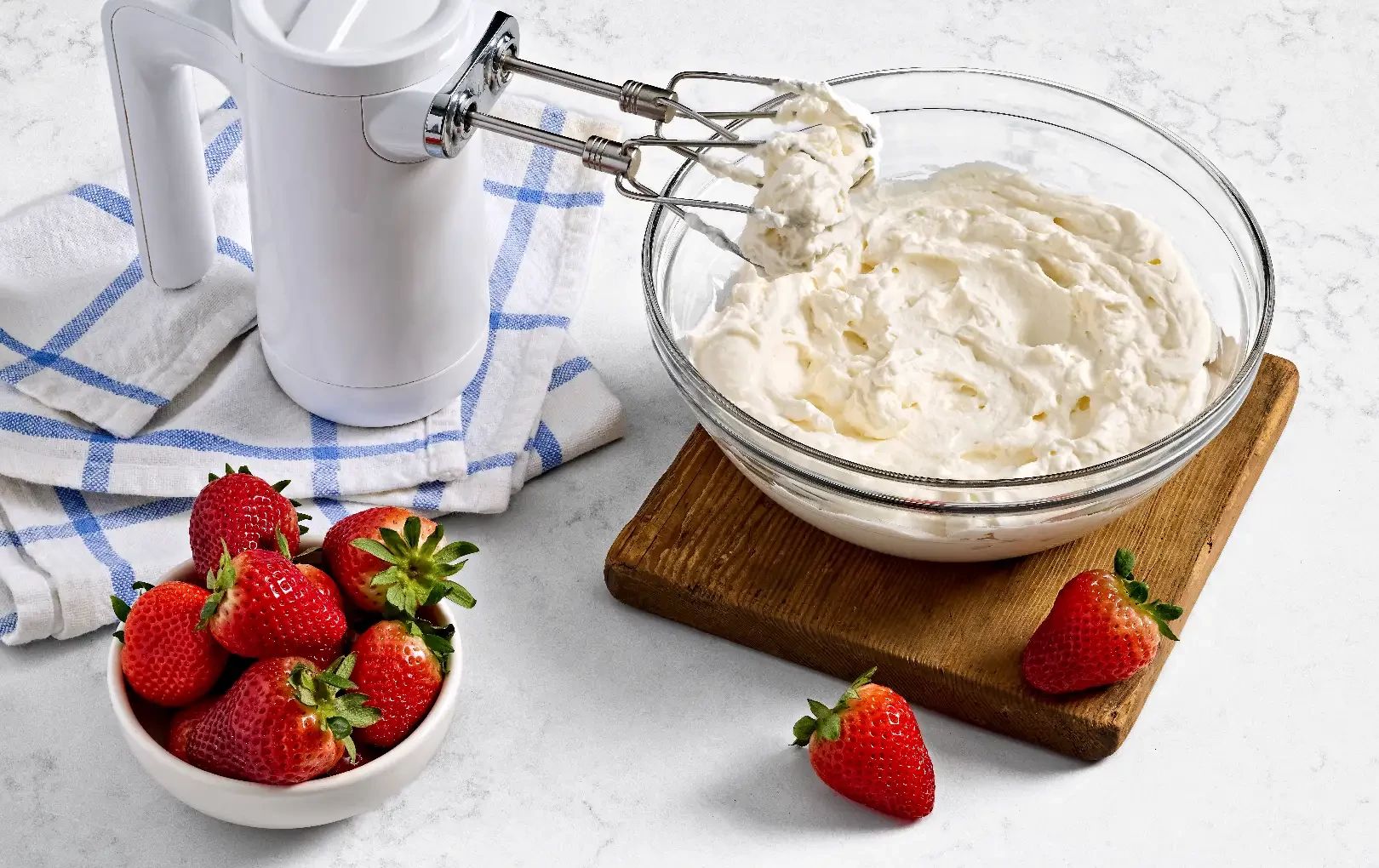 Whipped cream in mixing bowl with fresh strawberries on side
