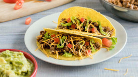 2 ground beef tacos on a plate with a side of guacamole