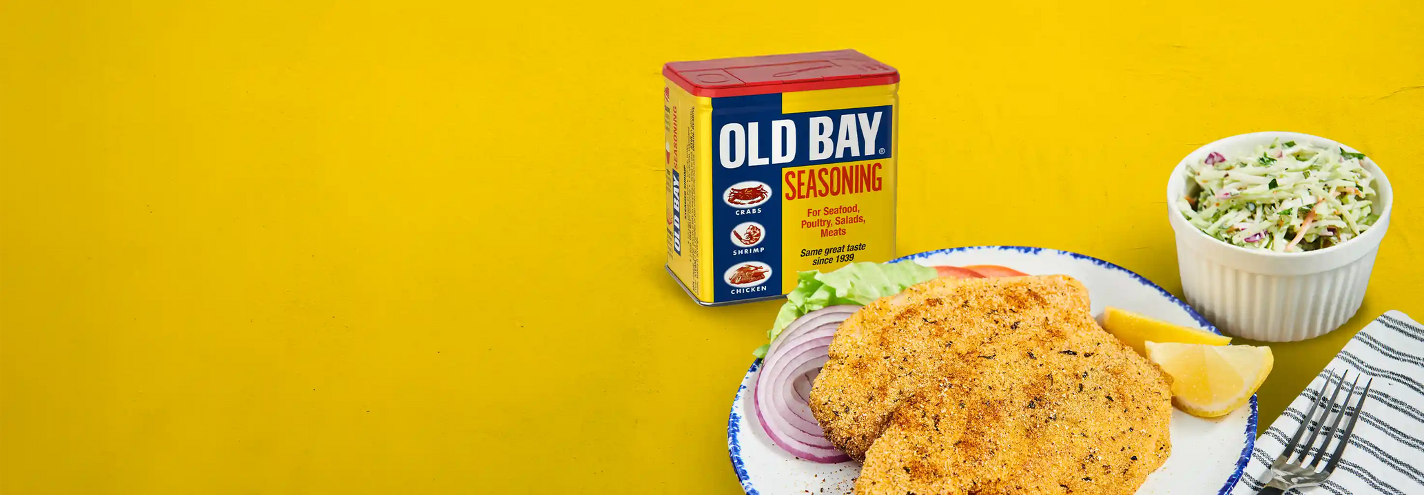 old bay seasoning on a plain yellow background next to a plate of old bay crusted fish and cole slaw