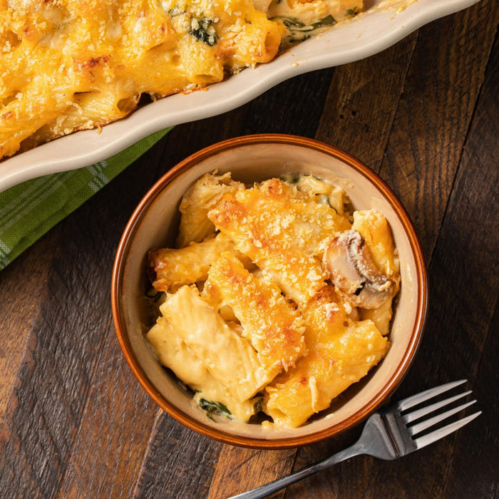 ['A bowl of macaroni and cheese with mushrooms and spinach.']
