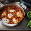 A close-up of a pan of shakshuka with eggs, peppers, and spices.