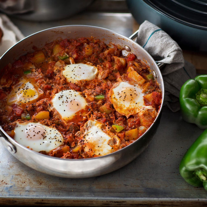 A close-up of a pan of shakshuka with eggs, peppers, and spices.