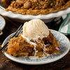 A slice of apple crumble topped with a scoop of vanilla ice cream.