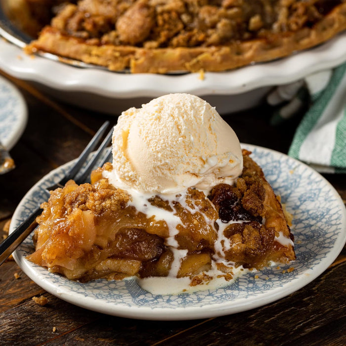 A slice of apple crumble topped with a scoop of vanilla ice cream.