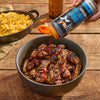 Mission BBQ Blue Ridge Smoky Mountain BBQ Sauce is being poured over grilled chicken wings in a bowl, with a side of macaroni and cheese.