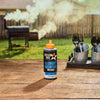 A bottle of Mission BBQ Blue Ridge Smoky Mountain BBQ Sauce sits on a wooden table with a smoker in the background.
