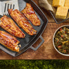 Four glazed fish fillets, coated in a rich sauce like Mission Bbq Blue Ridge Smoky Mountain 15 Oz, are presented in a black cast iron pan alongside a bowl of collard greens and cornbread on a rustic wooden table.