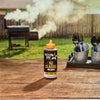 A bottle of Mission BBQ KC Classic BBQ Sauce sits on a wooden table with a smoker in the background.