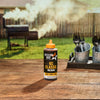 A bottle of Mission Bbq Kc Classic Bold Barbecue Sauce Plastic Squeeze Bottle 16 Oz sits on a wooden table in a backyard setting, with a smoking barbecue grill in the background.