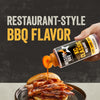 A hand squeezes a bottle of Mission Bbq Kc Classic Bold Barbecue Sauce Plastic Squeeze Bottle 16 Oz over a delicious-looking sliced meat sandwich on a dark plate.