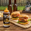 A bottle of Mission BBQ KC Classic BBQ Sauce is featured next to two burgers on a wooden board.