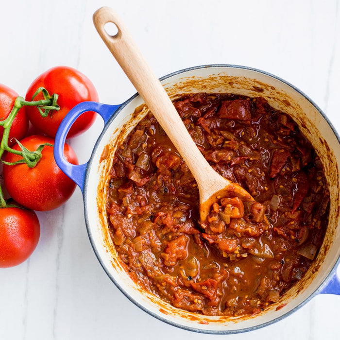 A pot of tomato sauce with a wooden spoon in it.