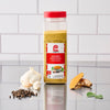 A bottle of Just Raita Seasoning Mix is displayed with garlic, peppercorns, turmeric, and a green leaf, highlighting its natural ingredients.