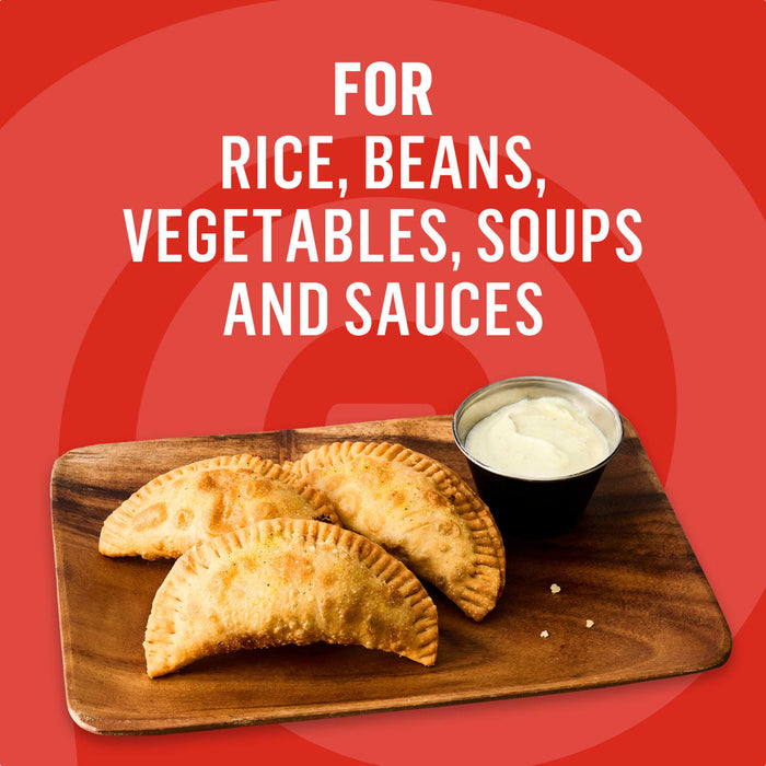 This image promotes a versatile product suitable for rice, beans, vegetables, soups, and sauces, showcasing three golden-brown empanadas served with a creamy dipping sauce on a wooden board.