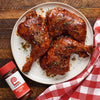 Three Lawry's seasoned chicken legs on a white plate with a red and white checkered napkin.
