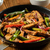 A skillet filled with sizzling fajitas, featuring strips of seasoned meat, colorful bell peppers, and red onions.