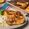 A plate of glazed chicken wings served with rice and green vegetables, alongside a baking sheet with more wings.