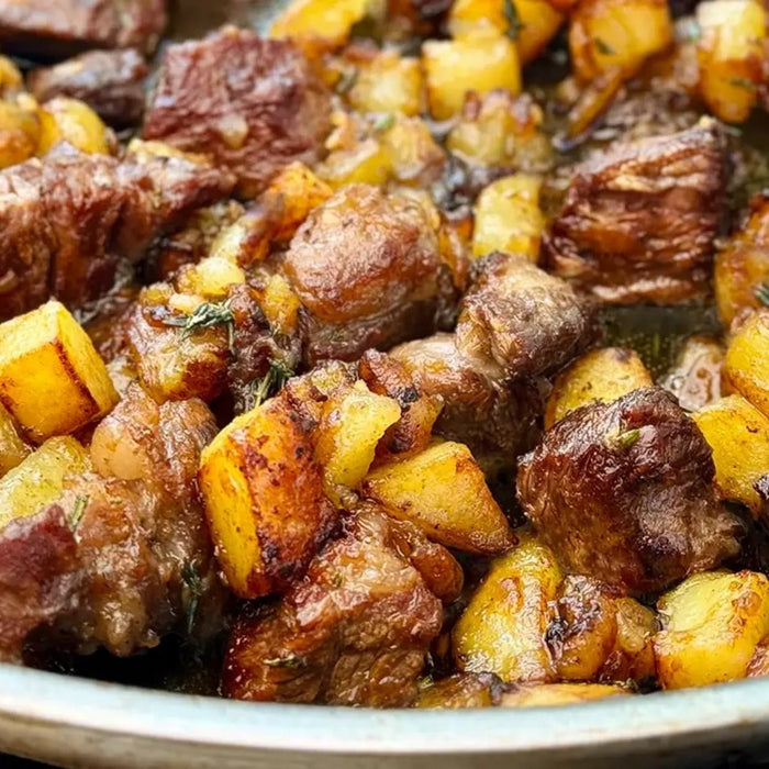 A close-up shot of a pan filled with golden-brown roasted potatoes and tender pieces of beef, creating a hearty and flavorful dish.
