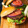 Two delicious-looking burgers with fresh toppings are displayed on a wooden board, ready to be enjoyed.