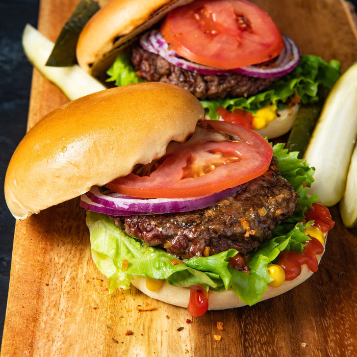 Two delicious-looking burgers with fresh toppings are displayed on a wooden board, ready to be enjoyed.